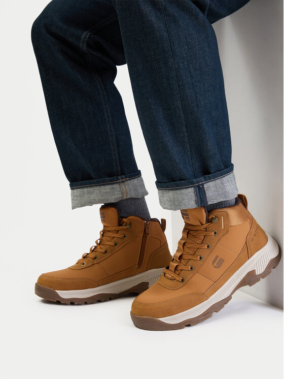 Model siedzący, na stopach widoczne buty outdoorowe, ujęcie z boku.