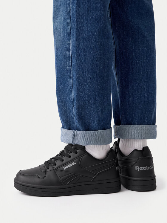 Model w spodniach prezentujący buty na stopach, ujęcie od dołu nóg.