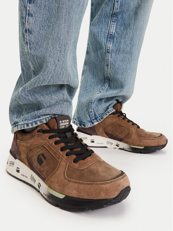 Model w spodniach prezentujący buty na stopach, ujęcie z góry na obuwie.